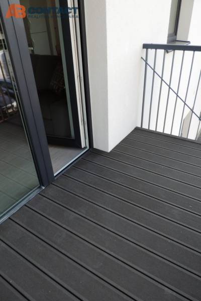 Balkon mit Holzboden in der Bodona-Straße, Teil eines Einzimmerapartments mit großem Fenster.