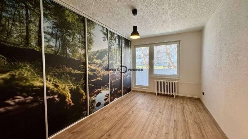 Ein Zimmer in einer 3-Zimmer-Wohnung mit einer großflächigen Tapete eines Waldes und einem Boden mit Holzdekor.