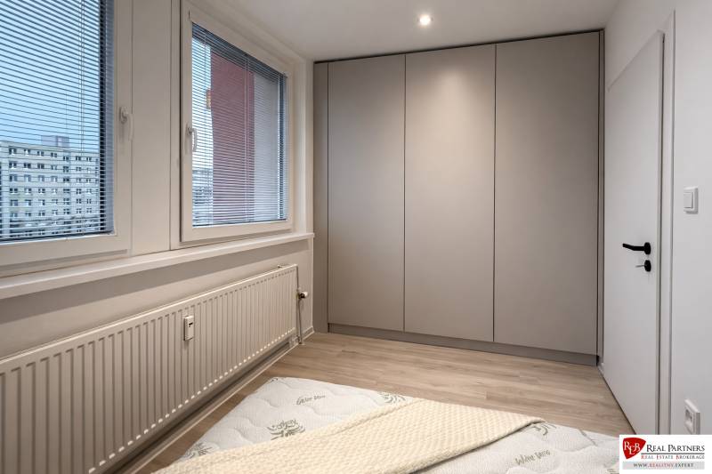 Schlafzimmer einer 2-Zimmer-Wohnung mit Einbauschrank, großem Fenster und Boden in Holzoptik.