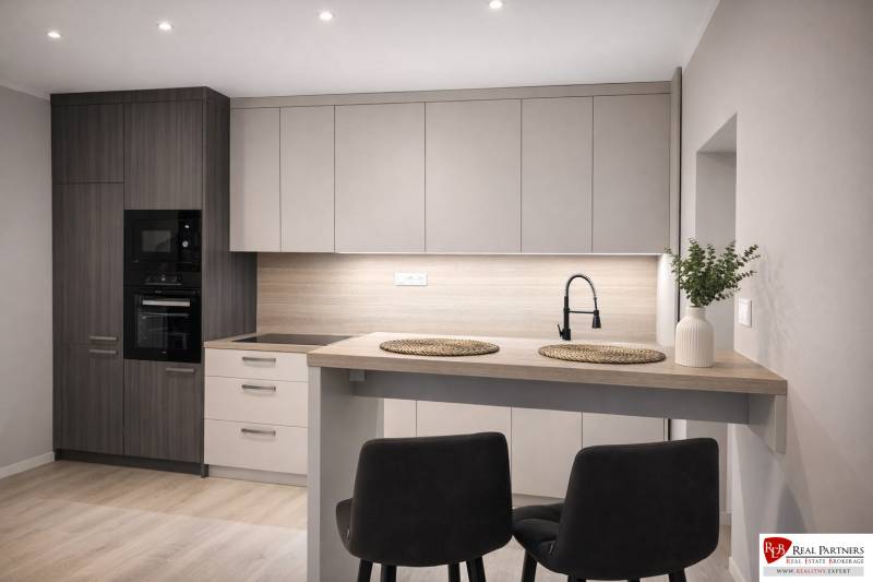 Küche in einer 2-Zimmer-Wohnung mit Holzboden, moderner Küchenzeile und Esstisch.