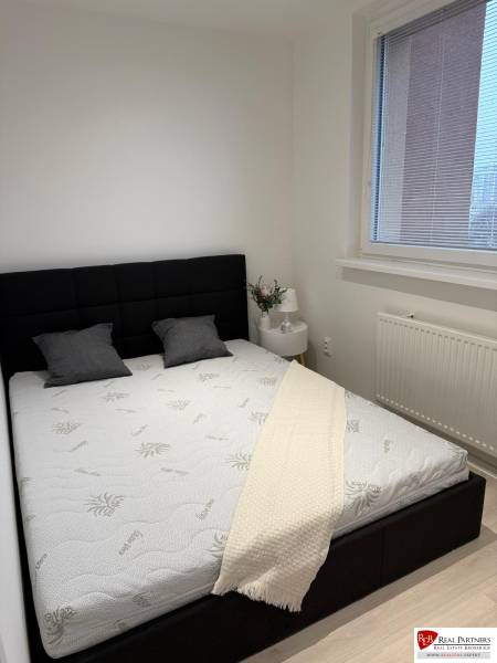 Schlafzimmer in einer 2-Zimmer-Wohnung mit schwarzem Kopfteil, weißer Bettdecke und Fenster mit Rollläden.