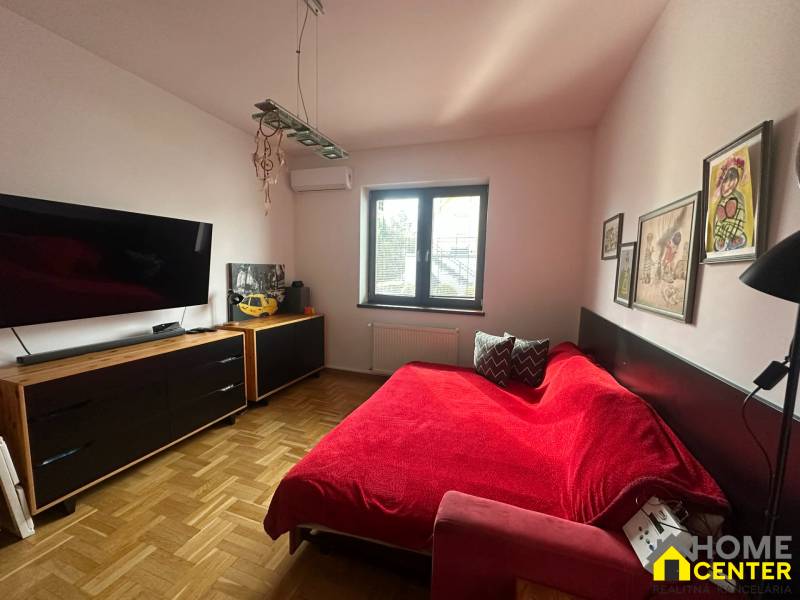 Ein Schlafzimmer in einem Einfamilienhaus mit einem roten Sofa, Kunstwerken und einem Boden in Holzoptik.