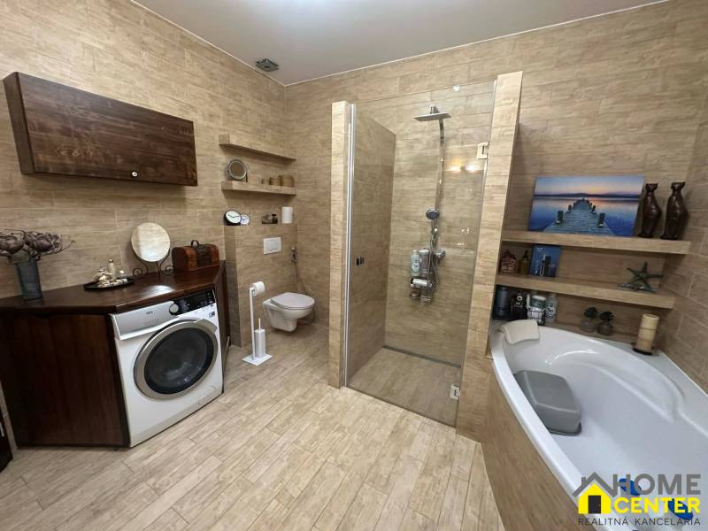 Badezimmer eines Einfamilienhauses mit Waschmaschine, Badewanne und Dusche, Boden mit Holzdekor.