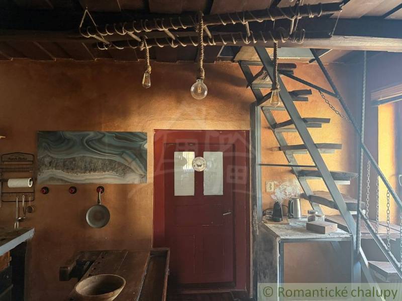 Innenraum eines Einfamilienhauses mit Holztreppe, rustikalem Tisch und künstlerischem Wandgemälde.