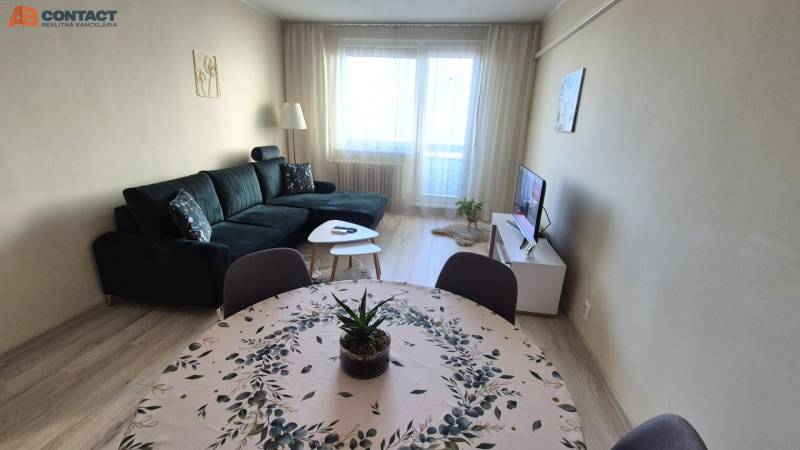 Wohnzimmer mit dunklem Sofa, Esstisch und Holzboden in einer Zweizimmerwohnung.