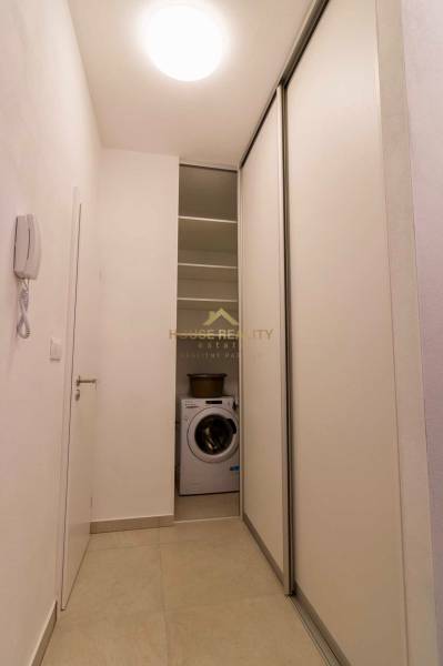 Ein enger Flur in einer Einzimmerwohnung mit einer Waschmaschine und Schiebetüren.