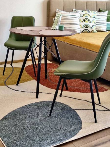 Innenraum einer Einzimmerwohnung mit einem bunten Teppich, einem Tisch und grünen Stühlen, Boden mit Dekor.