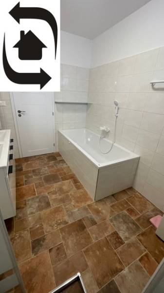Das Badezimmer im Einfamilienhaus hat eine Badewanne, weiße Fliesen und einen Boden mit Holzdekor.