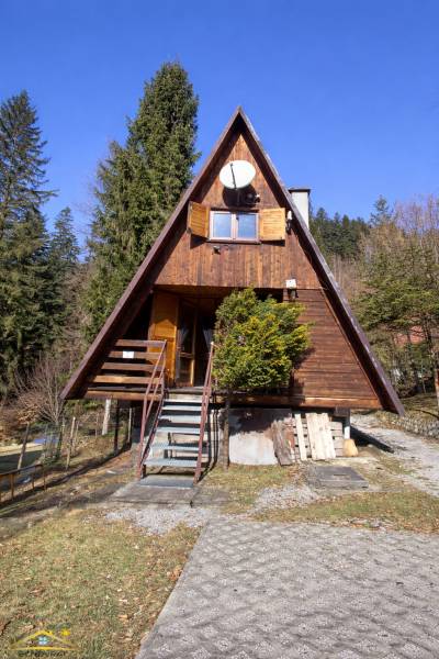 Eine Holzhütte in Oščadnica, umgeben von Grün und Nadelbäumen in sanfter Sonne.