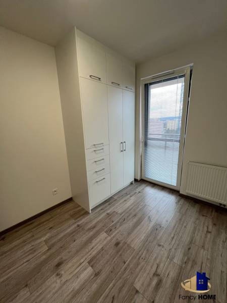 Ein Zimmer mit einem weißen Schrank, einem Boden in Holzoptik und Balkontüren in einer 3-Zimmer-Wohnung.