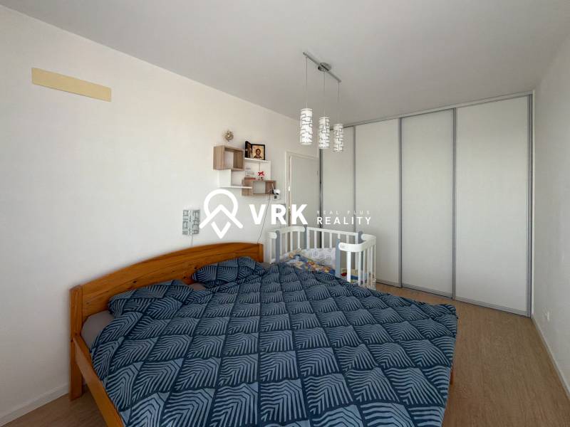 Schlafzimmer in einer 3-Zimmer-Wohnung mit einem Doppelbett, einem Kinderbett und einem Boden mit Holzdekor.