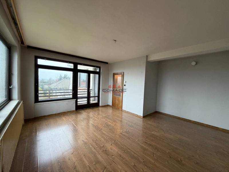 Ein Zimmer in einem Einfamilienhaus mit einem Boden in Holzoptik und großen Fenstern zum Garten.