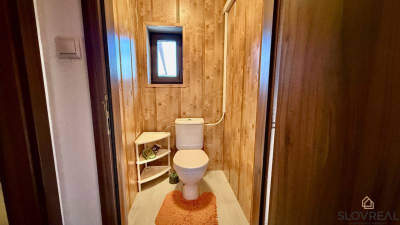 Toilette in einem Einfamilienhaus mit Holzverkleidung und kleinem Fenster.
