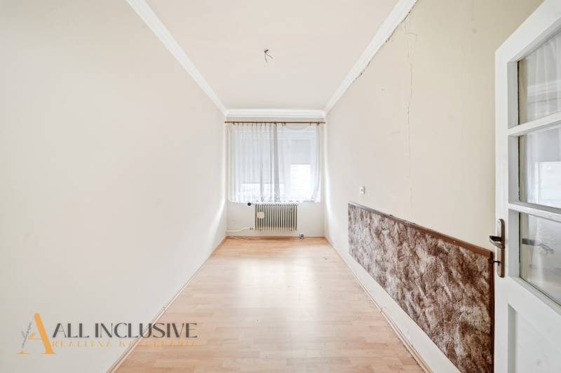 Ein schmaler Raum mit einem Holzboden, einem Fenster mit Vorhängen und einem Heizkörper.