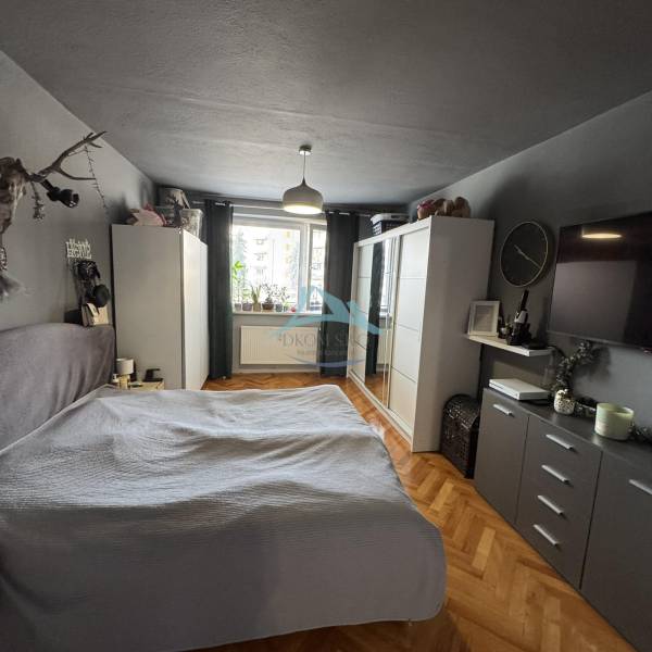 Schlafzimmer in einer 3-Zimmer-Wohnung mit Schrank, Bett und Boden in Holzoptik.
