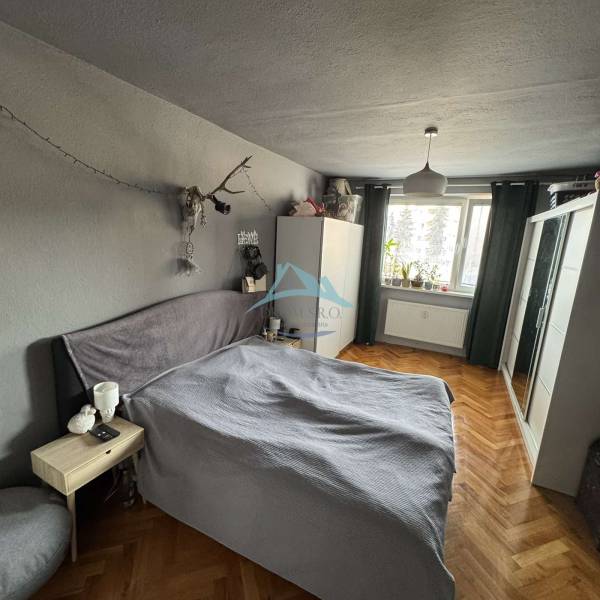 Schlafzimmer in einer 3-Zimmer-Wohnung mit Bett, Schrank und Boden in Holzoptik.