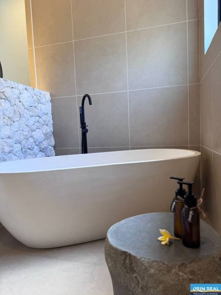 Ein Badezimmer in einem Einfamilienhaus mit einer Badewanne, einer mit Stein verkleideten Wand und dekorativen Fläschchen.