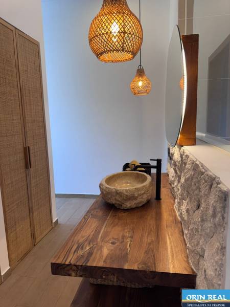 Innenraum eines Einfamilienhauses mit einem Waschbecken aus Stein, einer Holzplatte und Hängelampen.