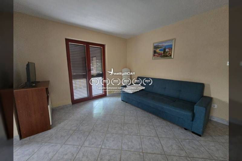 Wohnzimmer in einer besonderen Immobilie mit Sofa, TV-Schrank und gefliestem Boden.