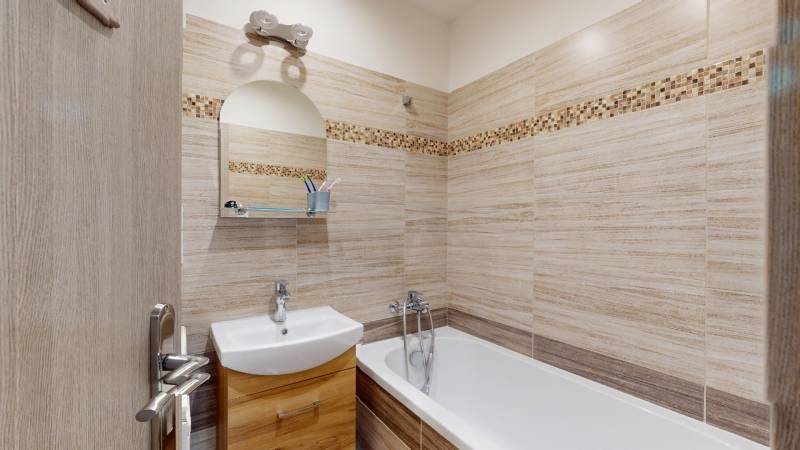 Badezimmer in einer 2-Zimmer-Wohnung mit hellen Fliesen und Badewanne, Schränke unter dem Waschbecken.