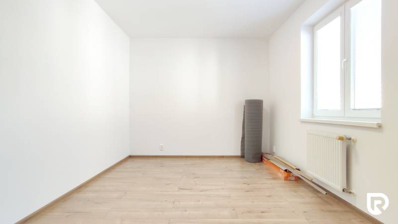 Ein leerer Raum in einer 2-Zimmer-Wohnung mit Holzboden und einem Heizkörper am Fenster.
