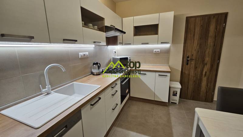 Die Küche in einer 2-Zimmer-Wohnung mit weißen Schränken und einem Boden in Holzoptik.