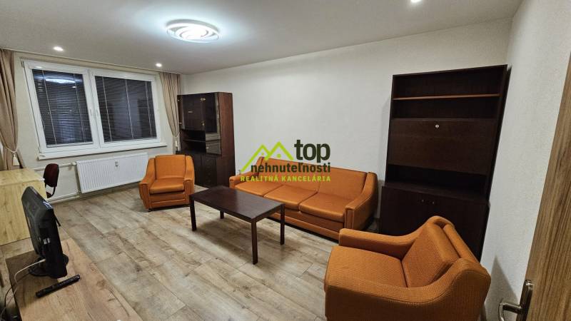 Wohnzimmer in einer Zweizimmerwohnung mit orangefarbenen Sofas und einem Boden in Holzoptik.