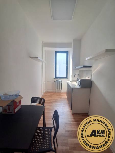 Ein schmales Büro mit einem schwarzen Tisch, Stühlen und einem Boden in Holzoptik.