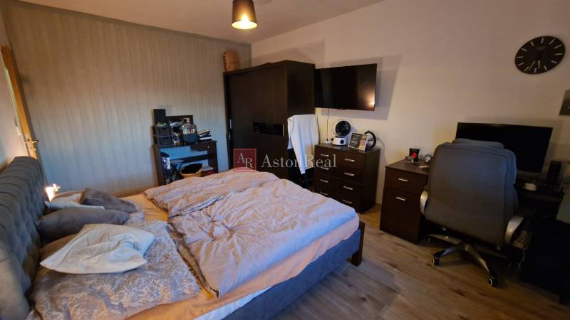 Schlafzimmer in einer 3-Zimmer-Wohnung mit einem komfortablen Bett, einem Schreibtisch und einem Boden mit Holzdekor.