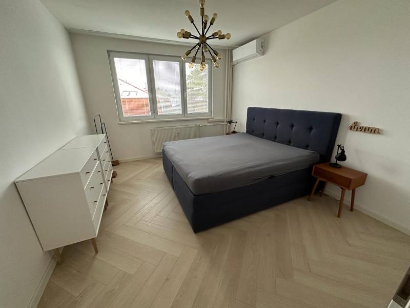 Schlafzimmer mit Bett, weißer Kommode, Holzboden und Hängelampe.