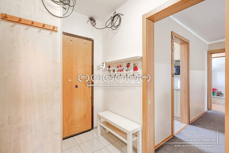 Eingangsflur in einer 4-Zimmer-Wohnung, weiße Wände, Kleiderhaken und Bank.