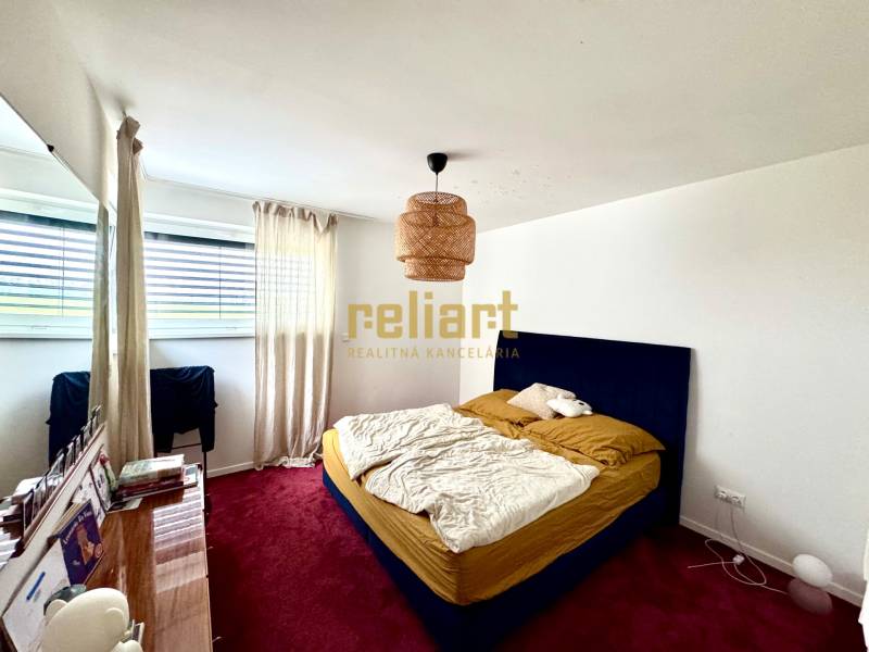 Ein Schlafzimmer in einem Einfamilienhaus mit rotem Teppich, blauem Bett und großem Fenster.