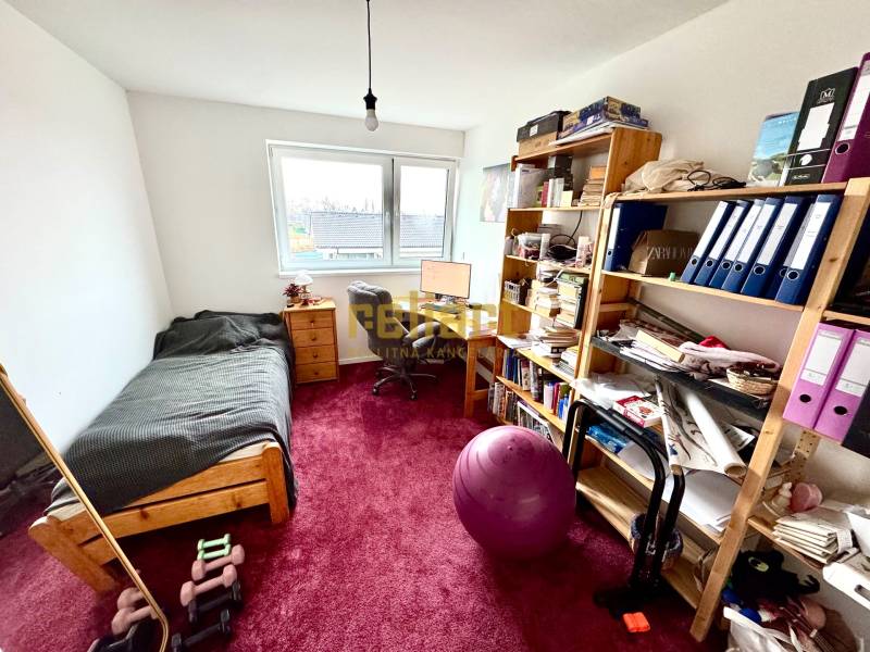 Ein Zimmer in einem Einfamilienhaus mit einem Tisch, einem Bett, Regalen und einem roten Teppich.