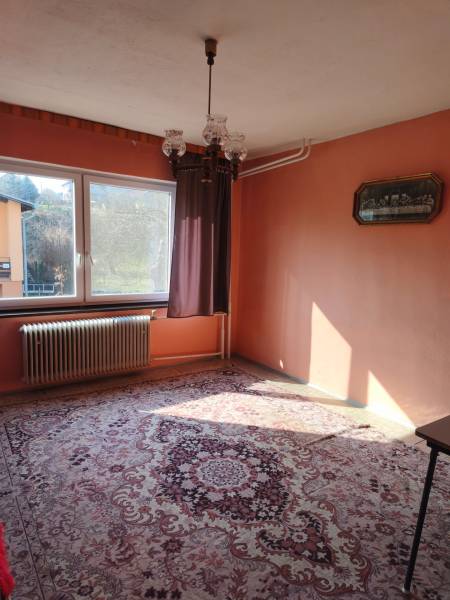 Ein Zimmer in einem Einfamilienhaus mit Teppich, Kronleuchter, Fenster und Heizkörper, warme farbige Wände.