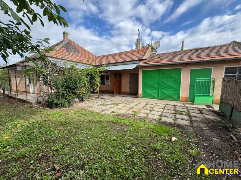 Garten und Terrasse bei einem Einfamilienhaus in Komárno mit Garagentoren und Gartenbewuchs.