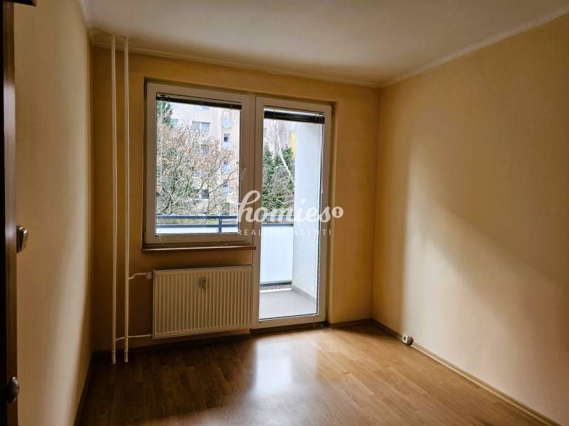 Ein leerer Raum in einer 3-Zimmer-Wohnung mit Holzdekorboden und verglasten Balkontüren.