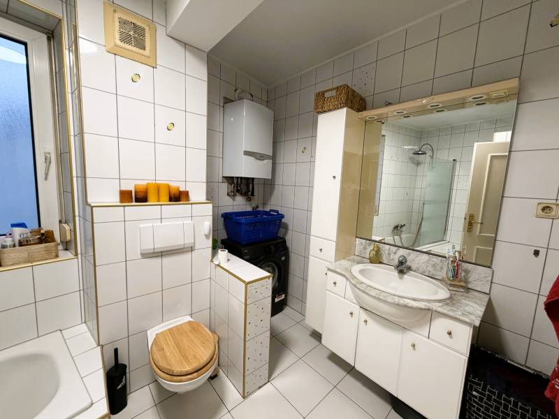 Badezimmer in einer 3-Zimmer-Wohnung mit Badewanne, Toilette und Waschmaschine, weiße Fliesen.