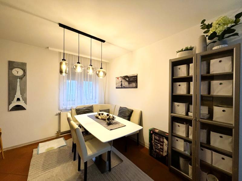 Esszimmer mit Tisch, Stühlen und Regal in einer 3-Zimmer-Wohnung mit dekorativer Beleuchtung.