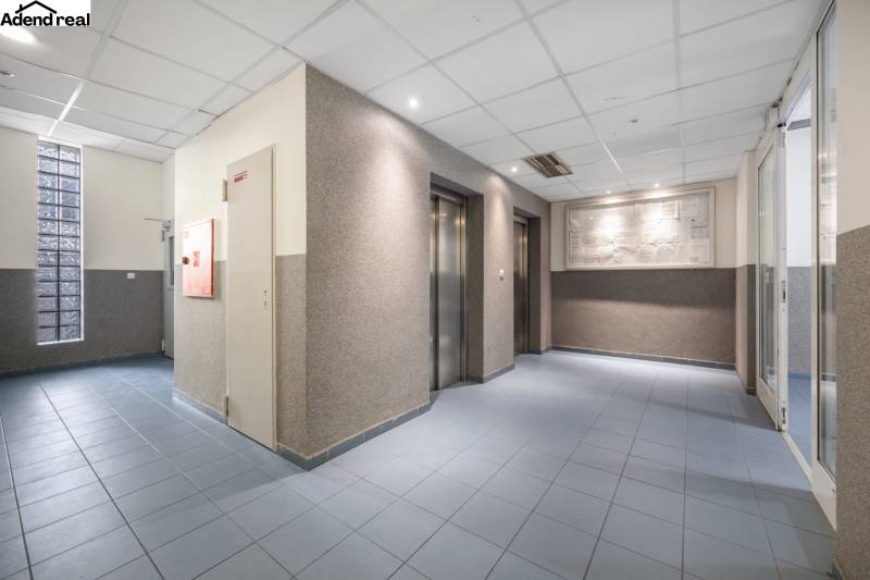 Eingangshalle mit Aufzügen, blauer Boden, beleuchtete Decken.