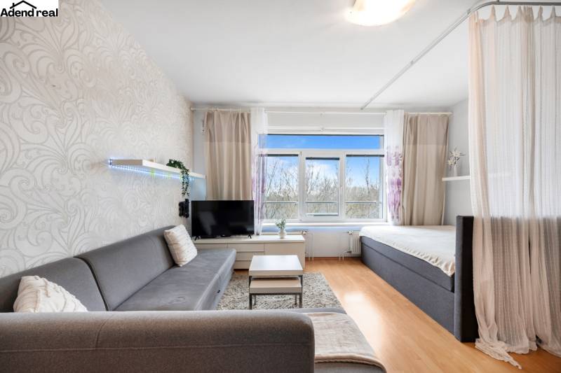 Wohnzimmer mit Sofa, Vorhang und Fernseher, Boden mit Holzdekor.