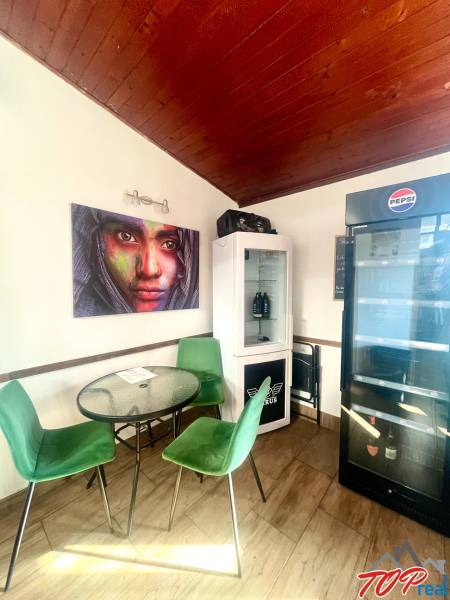 Gastronomische Räume mit Holzboden, grünen Stühlen, Bildern und Kühlschrank.