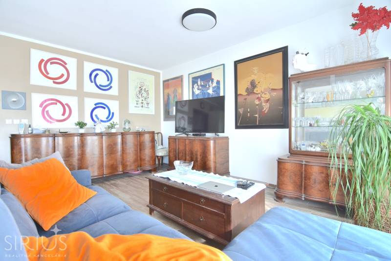 Wohnzimmer in einer 3-Zimmer-Wohnung mit Holzmöbeln, Boden mit Holzdekor und Bildern an den Wänden.