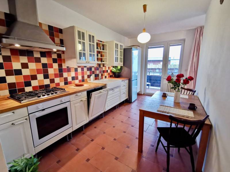 Küche in einer 4-Zimmer-Wohnung mit farbigen Fliesen, Tresen und Tisch mit Blumen.