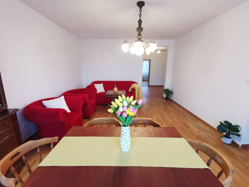 4-Zimmer-Wohnung mit roter Sitzgarnitur, Esstisch und Boden mit Holzdekor.