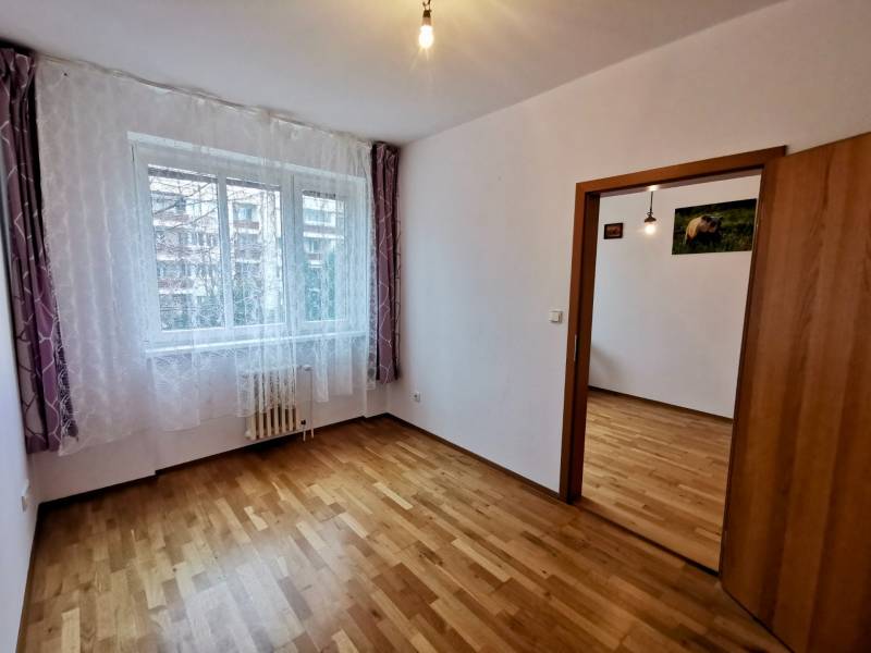 Ein Zimmer mit einem Holzboden in einer 4-Zimmer-Wohnung, helle Vorhänge am Fenster.