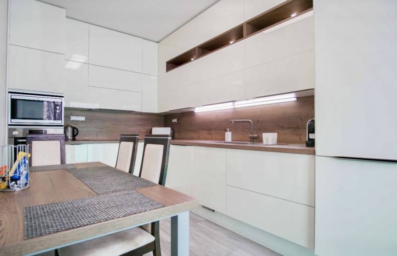 Küche in einer 3-Zimmer-Wohnung mit glänzenden Schränken und Holzwanddekoration.