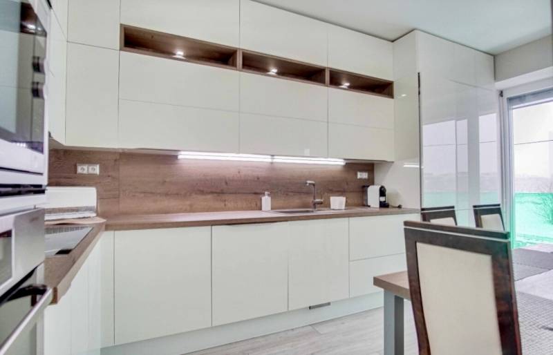 Küche in einer 3-Zimmer-Wohnung mit weißen Möbeln und einem Boden in Holzoptik.