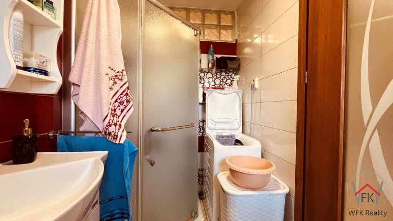 Badezimmer in einer 3-Zimmer-Wohnung mit Waschbecken, Duschkabine, Waschmaschine und Regal.