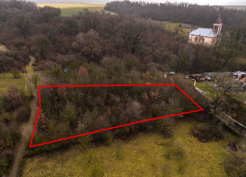 Erholungsgrundstücke in Gemerské Teplice, umgeben von Bäumen, mit einem historischen Kirchengebäude im Hintergrund.