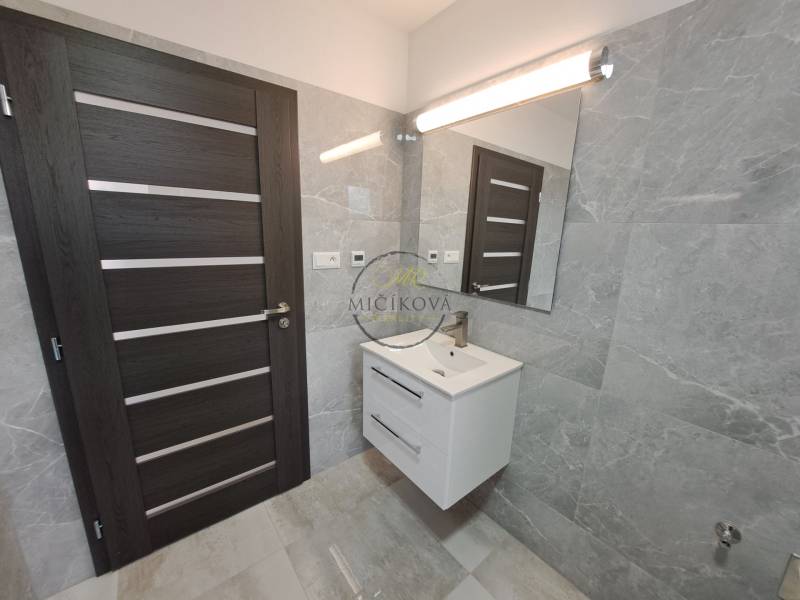 Badezimmer im Einfamilienhaus mit Waschbecken, Spiegel und dunkler Tür.